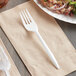 A white plastic fork on a napkin next to a plate of food.