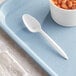 A Choice white plastic teaspoon on a blue tray next to a bowl of beans.