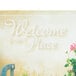 A blue metal counter with a Hoffmaster Welcome Paper Placemat with a sign that says "Welcome to our place" and flowers.