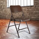 A brown National Public Seating metal folding chair in front of a brick wall.