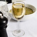 A close up of a Libbey white wine glass filled with wine on a table.