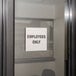 A Tablecraft stainless steel "Employees Only" sign on a glass door.
