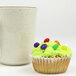 A white fluted baking cup with a cupcake with candy on top on a white surface.