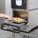 A person uses a Merrychef countertop oven to cook french fries in a pan on a school kitchen counter.
