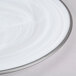 A close-up of a white Charge It by Jay alabaster glass charger plate with a silver rim.