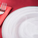 A white Charge It by Jay alabaster glass charger plate with a silver rim on a red tablecloth with a fork and knife.