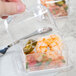 A hand holding a Fineline clear rectangular tray with shrimp in it.
