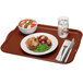 A brown Cambro rectangular fiberglass tray with food, a fork, and a knife on a napkin.