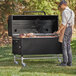 A man standing in front of a Backyard Pro charcoal and wood smoker grill with meat on it.