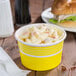 A yellow paper cup with food inside next to a sandwich