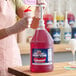 A large jug of Carnival King watermelon snow cone syrup with a pump dispenser being used to flavor a snow cone.