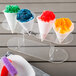 A row of colorful snow cones with orange, white, blue, and green snow cone syrup.