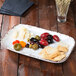 A white irregular rectangular platter with olives, cheese, and crackers on a table.