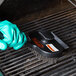 A person using a Chef Master grill cleaning brush with dual handles to clean a grill.