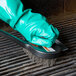 A gloved hand using a Chef Master grill cleaning brush to clean a grill.