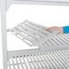 A hand holding a white shelf from a Cambro Camshelving Premium Add On Unit.