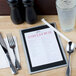 A Menu Solutions Alumitique aluminum menu board on a table with a fork and a glass of water.