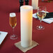 A white candle on a table with wine glasses.