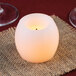 A Sterno white wax mini hurricane candle on a burlap surface with wine glasses.