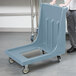 A person pushing a blue plastic Cambro dolly with wheels.