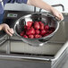 A person washing red potatoes in a Vollrath stainless steel colander.