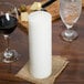 A white Sterno wax pillar candle on a table next to a glass of wine.