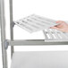 A hand placing a tray on a white Cambro Camshelving® Elements add-on shelf with vented and solid shelves.