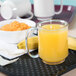 A clear GET Tritan mug filled with orange juice on a table with a bowl of fruit.