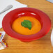 A red Sensation melamine bowl of orange soup with a leaf on top.