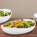 A table with two Osslo white melamine bowls filled with salad.