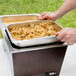 A person holding a tray of food in a Sterno Copper Vein stackable chafer.