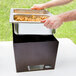 A person putting food into a Sterno Copper Vein stackable chafer on a table outdoors.