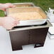A person using a Sterno Copper Vein chafer to serve food outdoors.