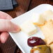 A hand holding a GET White Square Melamine Plate with cheese, olives, and crackers.