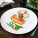 A Libbey Porcelana coupe plate with a piece of salmon and green beans on a table.