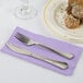 A fork and knife on a Luscious Lavender purple paper dinner napkin next to a plate of food.