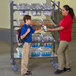 A woman in a red shirt hands a box to a boy using a Cambro Camshelving® Flex Station.