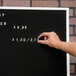 A person pointing to a black Aarco felt message board with white letters.