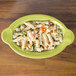 A lemongrass green Fiesta oval casserole dish filled with pasta and vegetables on a wood table.