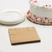 A white cake with red sprinkles next to a stack of Creative Converting Glittering Gold beverage napkins.