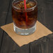 A glass of ice tea with a straw on a brown Creative Converting Glittering Gold beverage napkin.