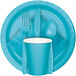 A blue plate with a Bermuda Blue Creative Converting beverage napkin, a Bermuda Blue plastic cup with a white lid, and Bermuda Blue cutlery.