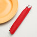 A fork in a red Creative Converting Classic Red dinner napkin next to a plate.