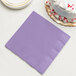 A Creative Converting Luscious Lavender purple paper napkin on a stack of plates with a white cake on top.