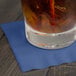 A glass of liquid with ice and a straw on a navy blue Creative Converting beverage napkin.