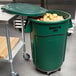 A green Rubbermaid BRUTE trash can with a lid and dolly holding potatoes.
