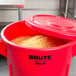 A red Rubbermaid BRUTE 55 gallon trash can with a lid full of food.