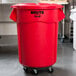 A red Rubbermaid BRUTE trash can on wheels.