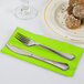 A knife and fork on a Fresh Lime Green paper dinner napkin next to a plate of food.