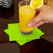 A hand holding a glass of orange juice with a lime green beverage napkin on the table.